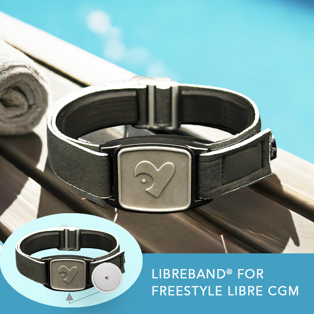 A stylish Freestyle Libre 2 CGM sports and swim armband with a pewter heart design on a neoprene strap, displayed by a poolside.