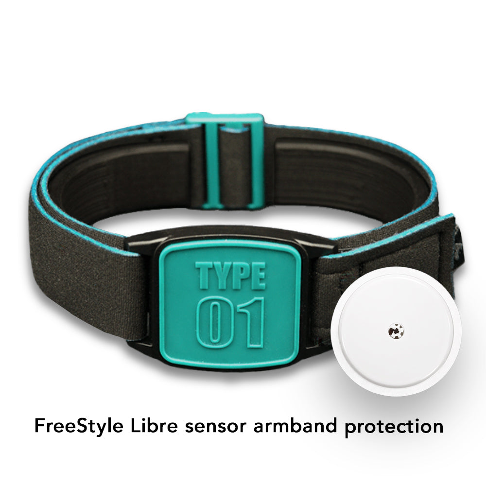A teal and black neoprene armband labeled 'TYPE 01' designed to secure a FreeStyle Libre 2 CGM sensor, displayed on a wooden table alongside a white towel. Close up inset of armband and sensor.