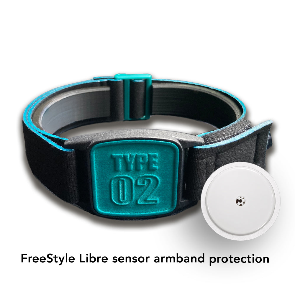 A Freestyle Libre 2 CGM sports and swim armband in teal and black, placed on a wooden surface near a white towel and pool in background.