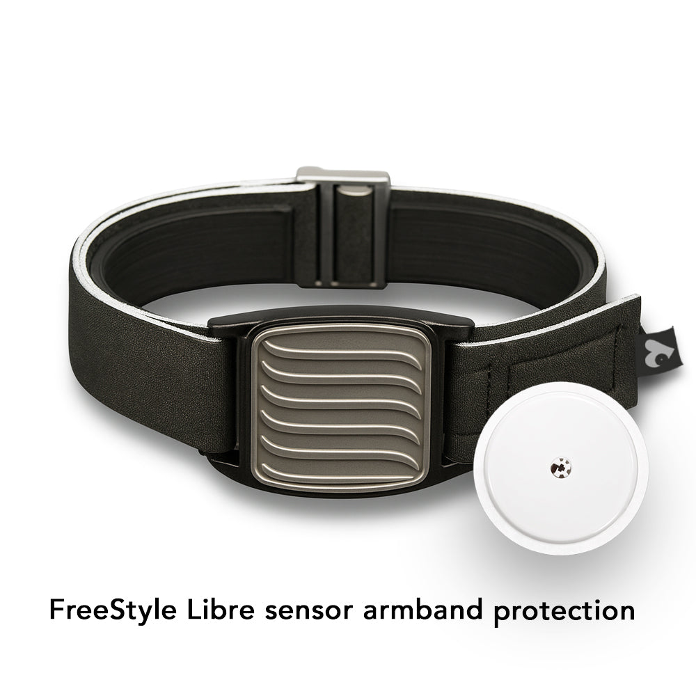 A pewter wave design Freestyle Libre 2 CGM sports and swim armband with a black neoprene strap, displayed on a wooden surface with a reflective shadow below.