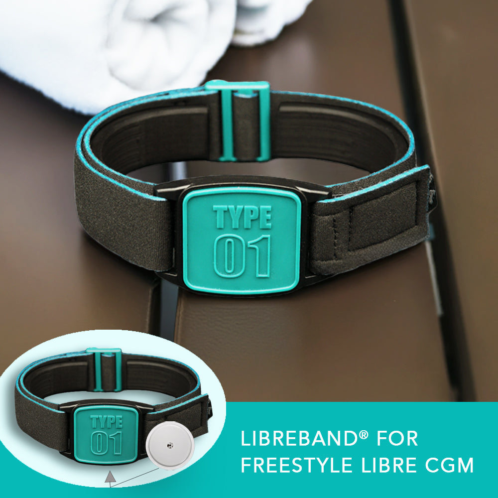 A teal and black neoprene armband labeled 'TYPE 01' designed to secure a FreeStyle Libre 2 CGM sensor, displayed on a wooden table alongside a white towel. Close up inset of armband and sensor.