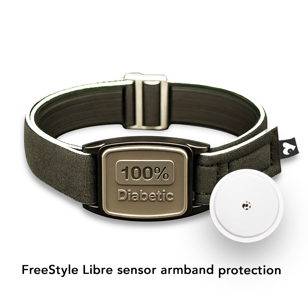 A pewter-colored Freestyle Libre 2 CGM sports and swim armband with a black neoprene strap, displayed on a wooden surface near a pool.